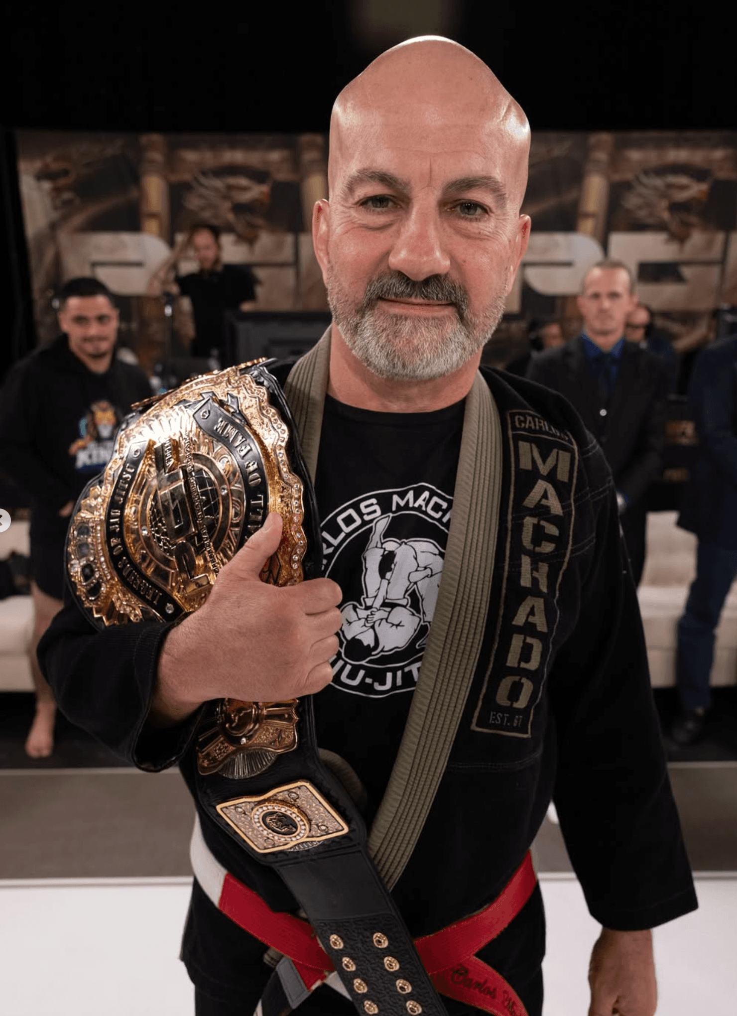 Carlos Machado smiling while holding the PGF Hall of Fame belt.